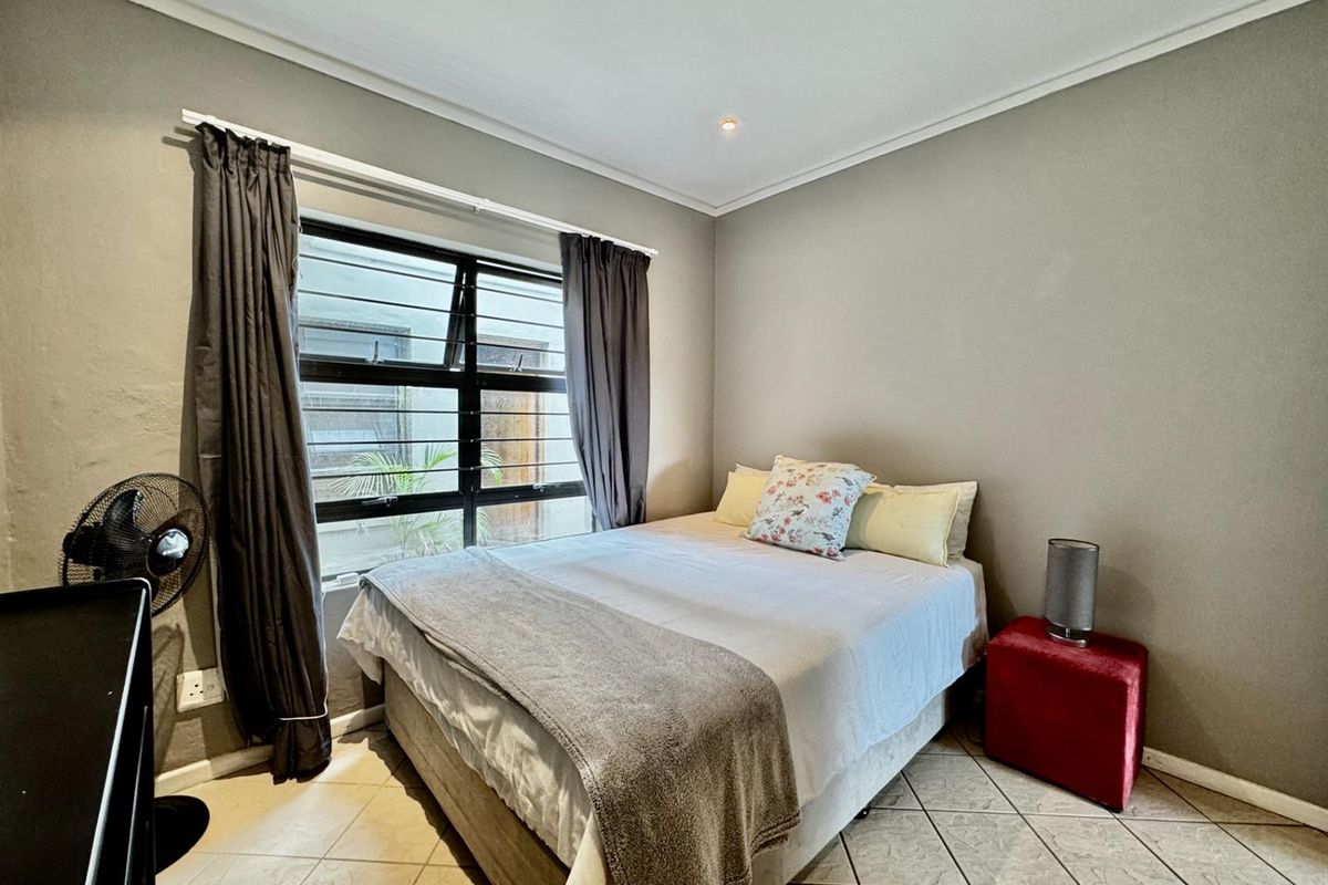A functional bedroom featuring tiled flooring, neutral wall tones, and a large window with security bars, providing natural light and ventilation.