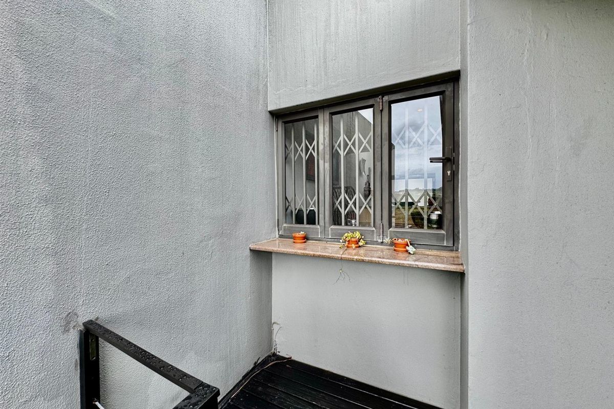 Exterior view of a townhouse wall featuring a window with security bars and a stone sill, adjacent to a staircase.