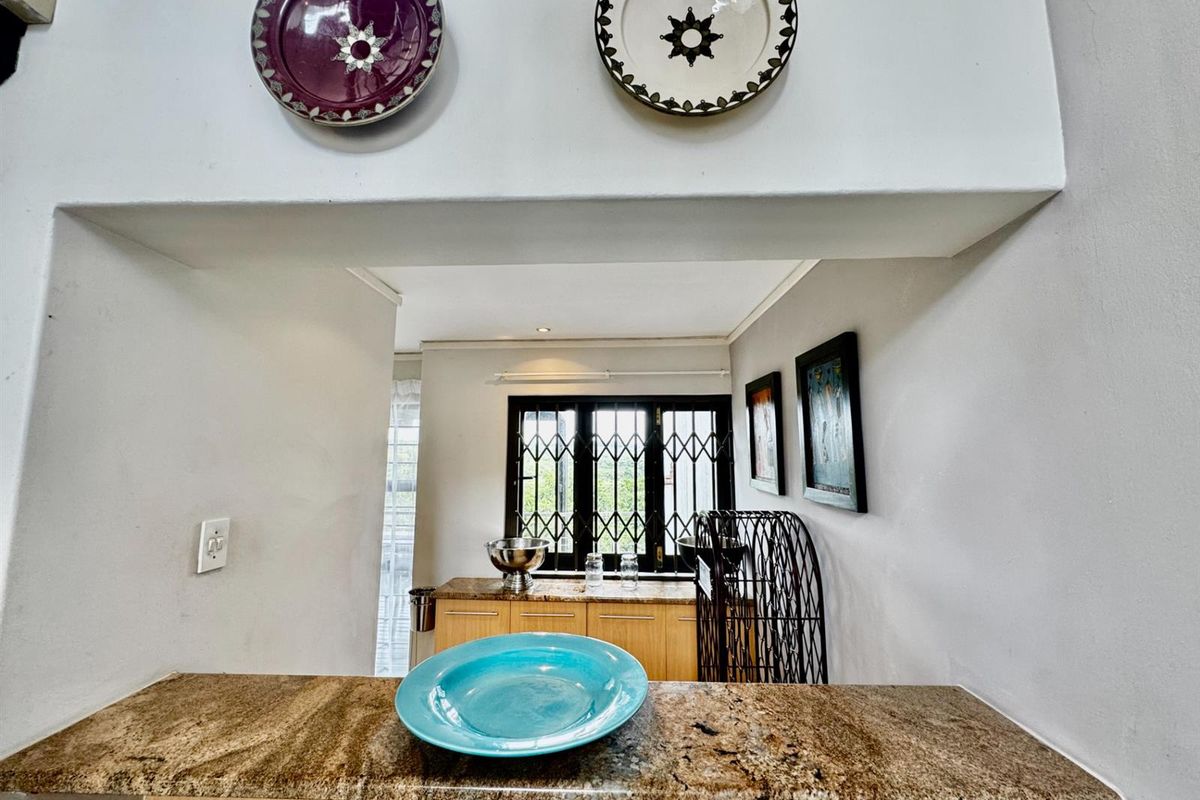 A view from a granite-topped breakfast bar looking into a kitchen area featuring light wood cabinetry and security bars on the window.