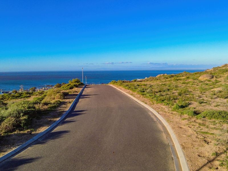 A scenic view of a paved road leading towards the ocean, showcasing the coastal landscape and natural terrain of the vacant residential land.