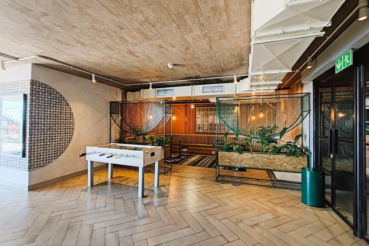 A modern communal recreation area featuring exposed concrete ceilings, herringbone tiled flooring, and integrated industrial-style lighting and ventilation systems.