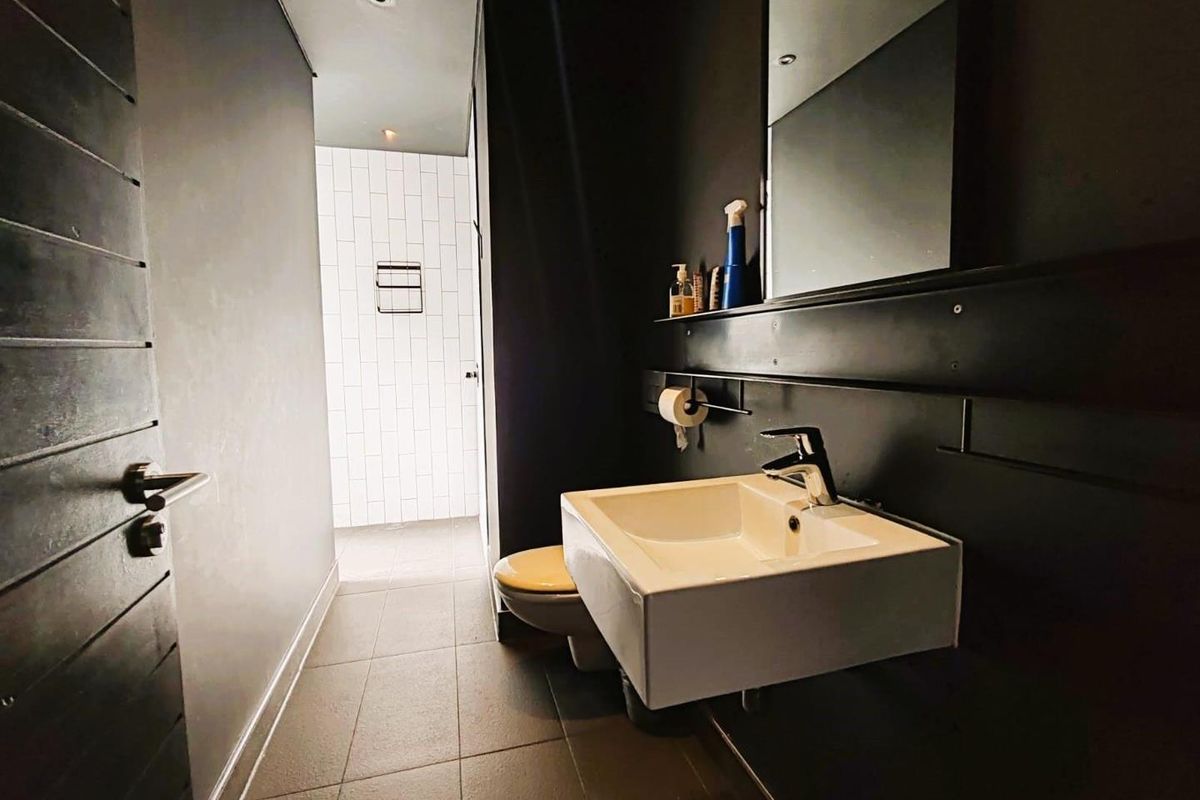 Modern bathroom featuring a wall-mounted basin, dark feature wall, large mirror, and tiled flooring, leading to a separate shower area.