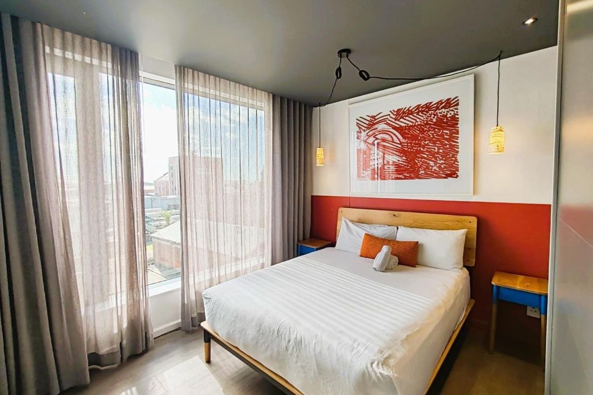 A modern bedroom featuring floor-to-ceiling windows with sheer curtains, recessed ceiling lighting, and a bold accent wall.