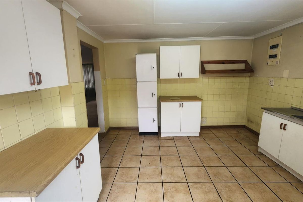 A dated kitchen featuring tiled walls, ceramic floor tiles, and basic white cabinetry with laminate countertops, offering potential for modernization.