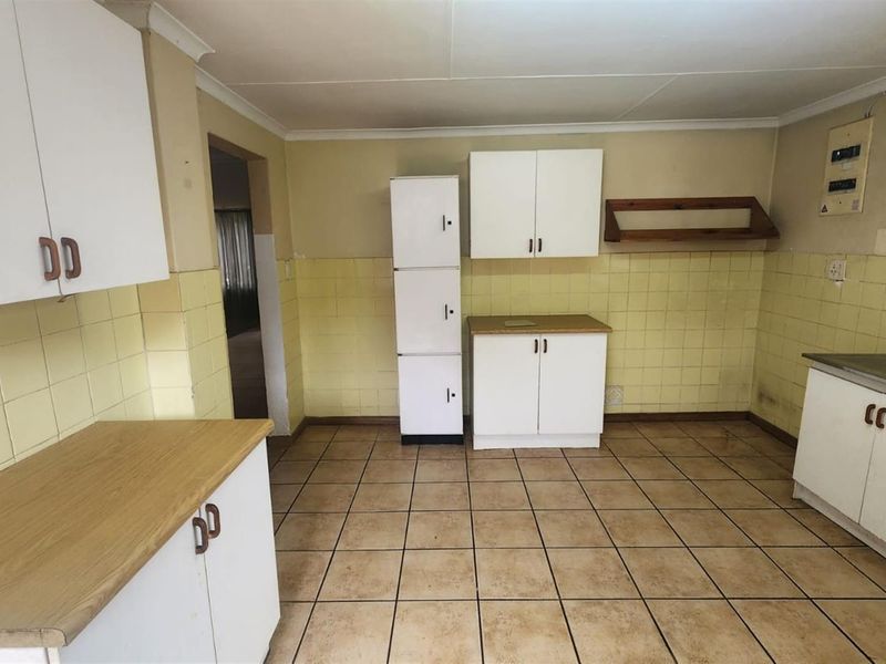 A dated kitchen featuring tiled walls, ceramic floor tiles, and basic white cabinetry with laminate countertops, offering potential for modernization.