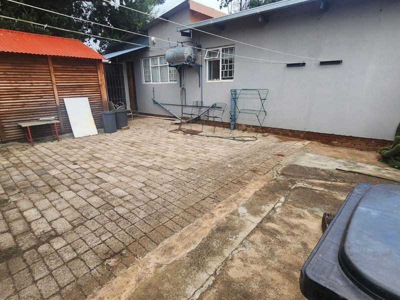 Rear exterior area featuring paved courtyard, timber storage shed, and exposed exterior plumbing fixtures against the main building wall.