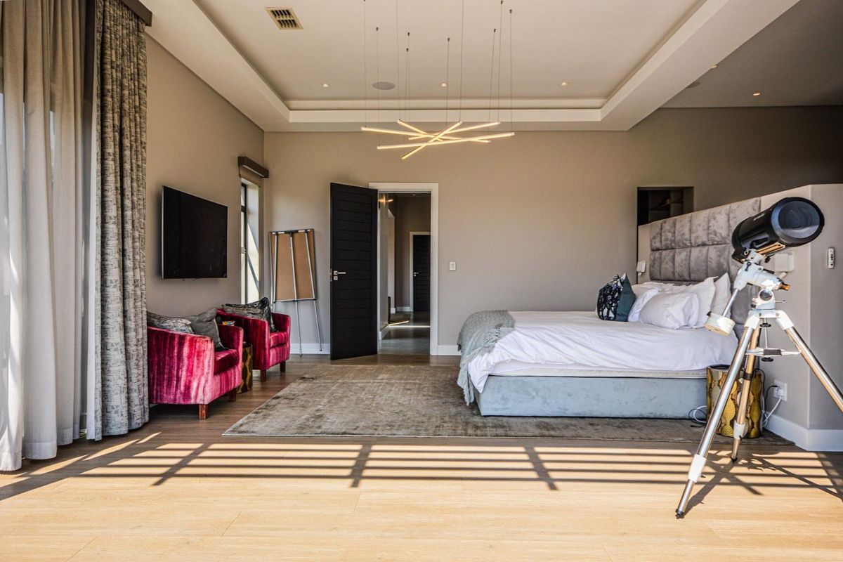 Spacious master bedroom featuring a recessed tray ceiling, modern pendant lighting, timber flooring, and direct access to an adjoining hallway.