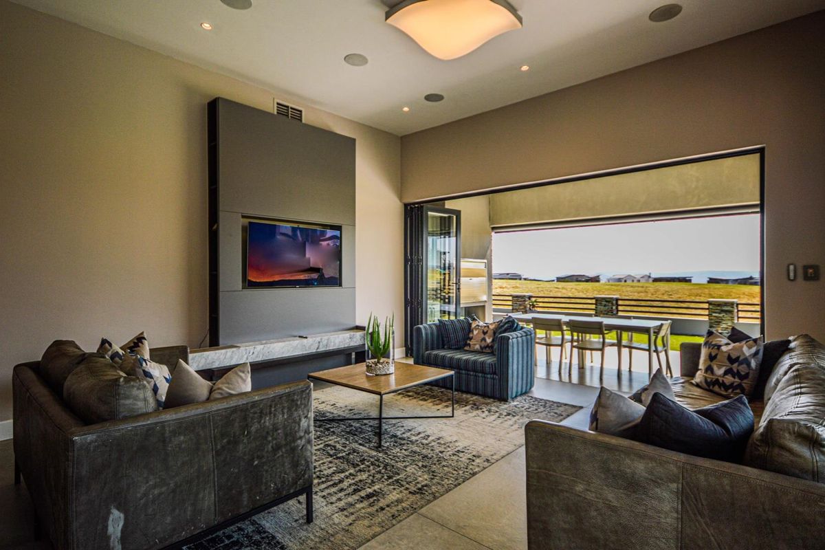 Modern living room featuring a built-in media wall, recessed ceiling lighting, and large sliding doors opening onto a covered patio with scenic views.