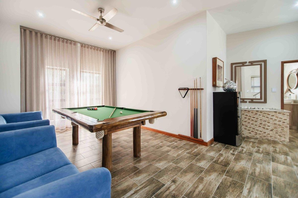A spacious entertainment room featuring wood-look tile flooring, recessed lighting, a ceiling fan, and a built-in bar area with stone cladding.
