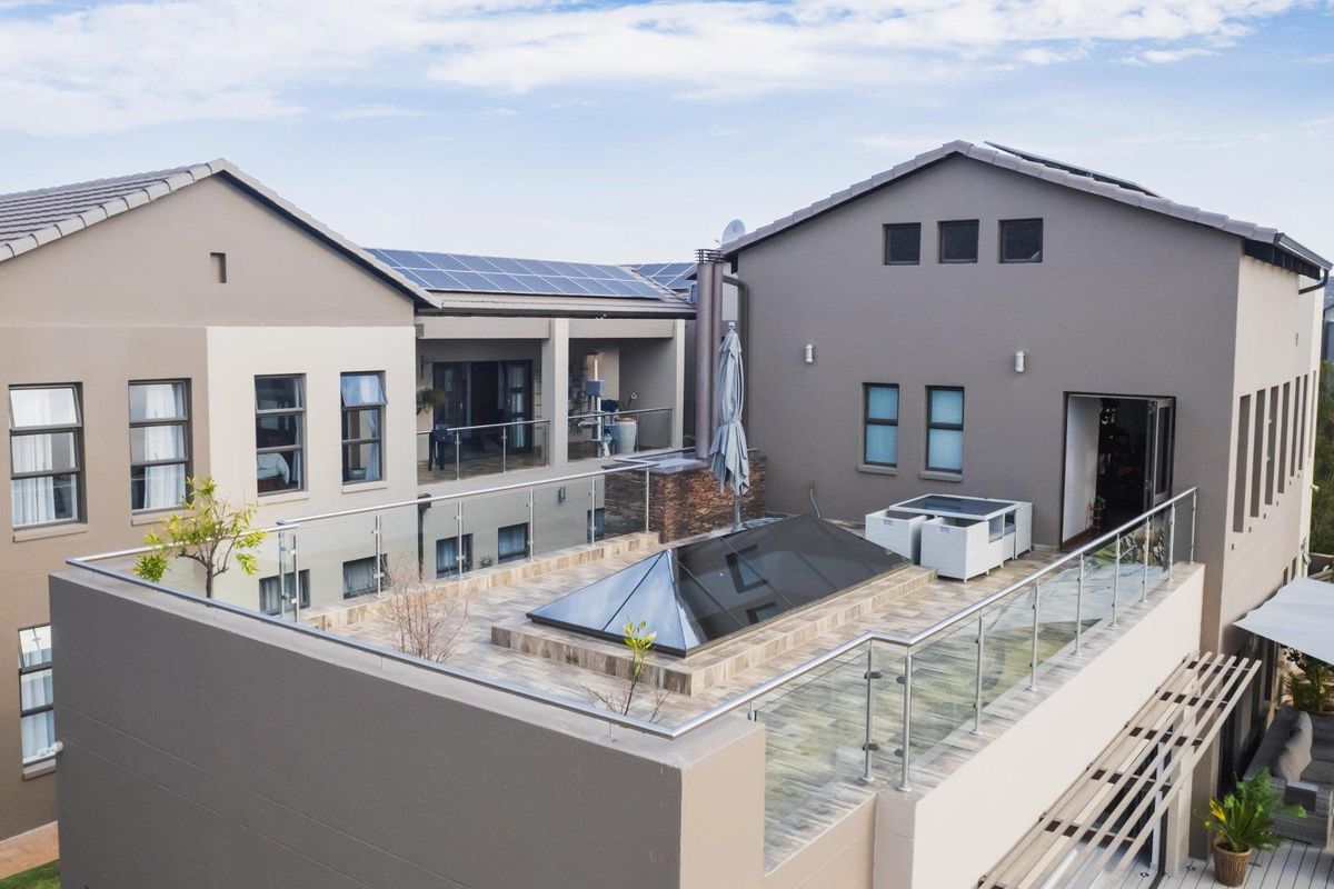 Elevated view of a modern residential property featuring a spacious rooftop terrace with glass balustrades, tiled flooring, and a central skylight structure.