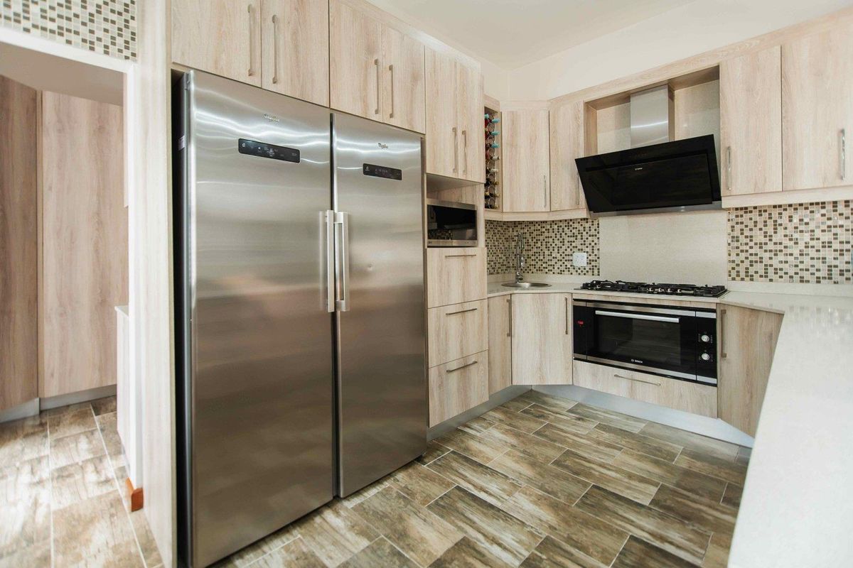 Modern kitchen featuring light wood-grain cabinetry, mosaic tile backsplash, built-in oven, gas cooktop, extractor fan, and stainless steel side-by-side refrigerator.