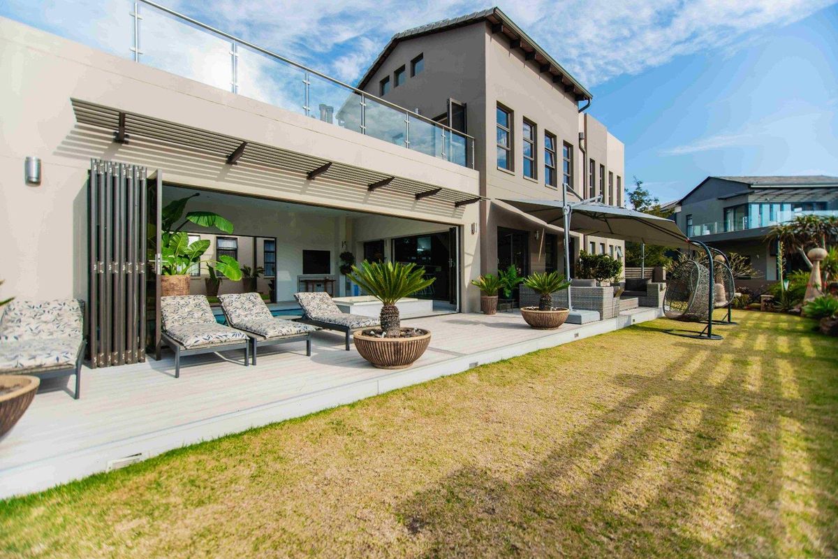 A spacious rear exterior view featuring a modern patio with folding doors, glass balcony railings, and a well-maintained garden area.
