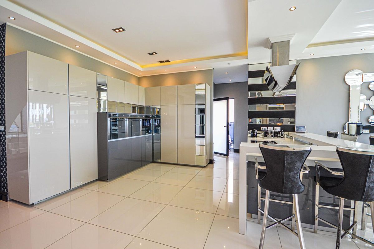 Modern kitchen featuring high-gloss cabinetry, integrated appliances, a breakfast bar, recessed ceiling lighting, and polished floor tiles.