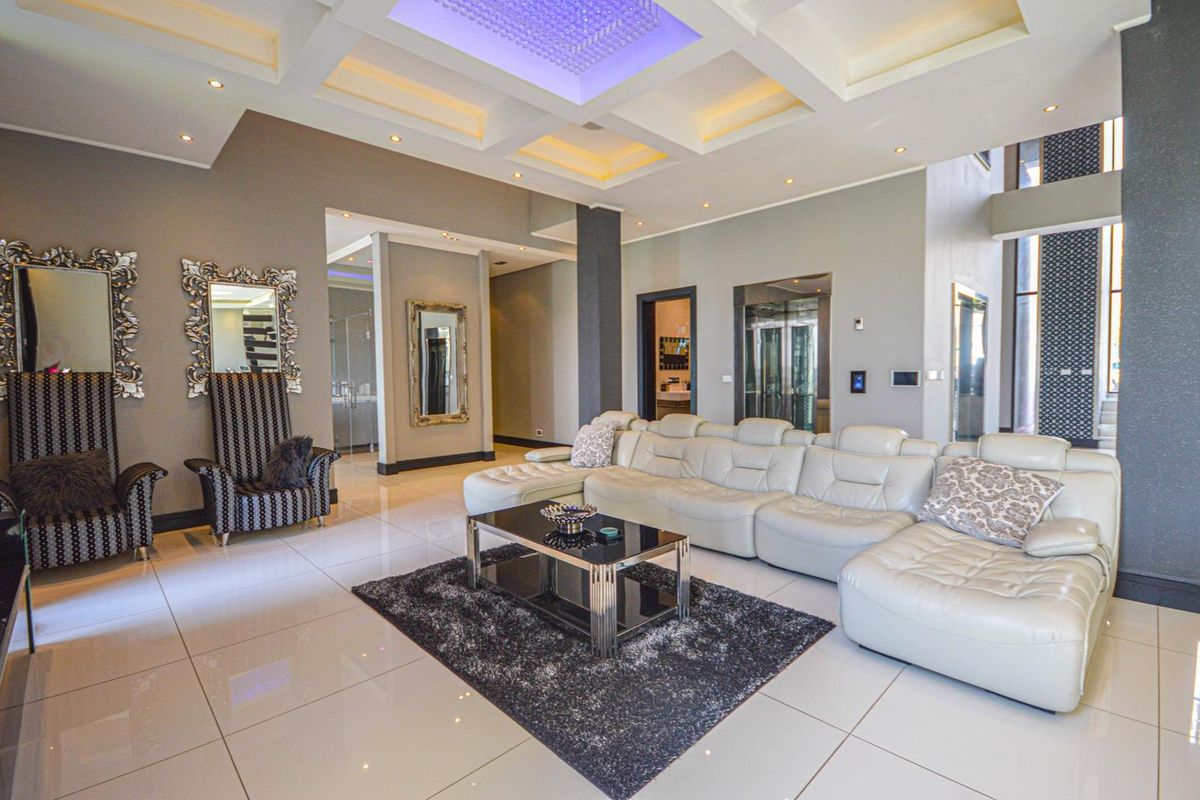 Spacious living area featuring a coffered ceiling with recessed lighting, polished tile flooring, and a modern glass elevator installation.