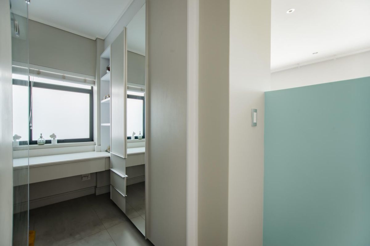 A modern bedroom featuring built-in cabinetry, a desk area, and a mirrored wardrobe, finished with neutral tones and recessed lighting.