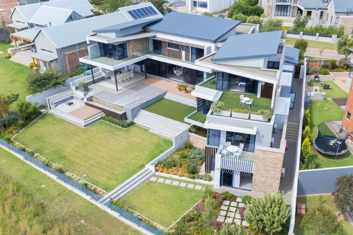 Aerial view of a modern multi-level residential property featuring tiered landscaping, a spacious rear patio, integrated solar panels, and contemporary architectural design.