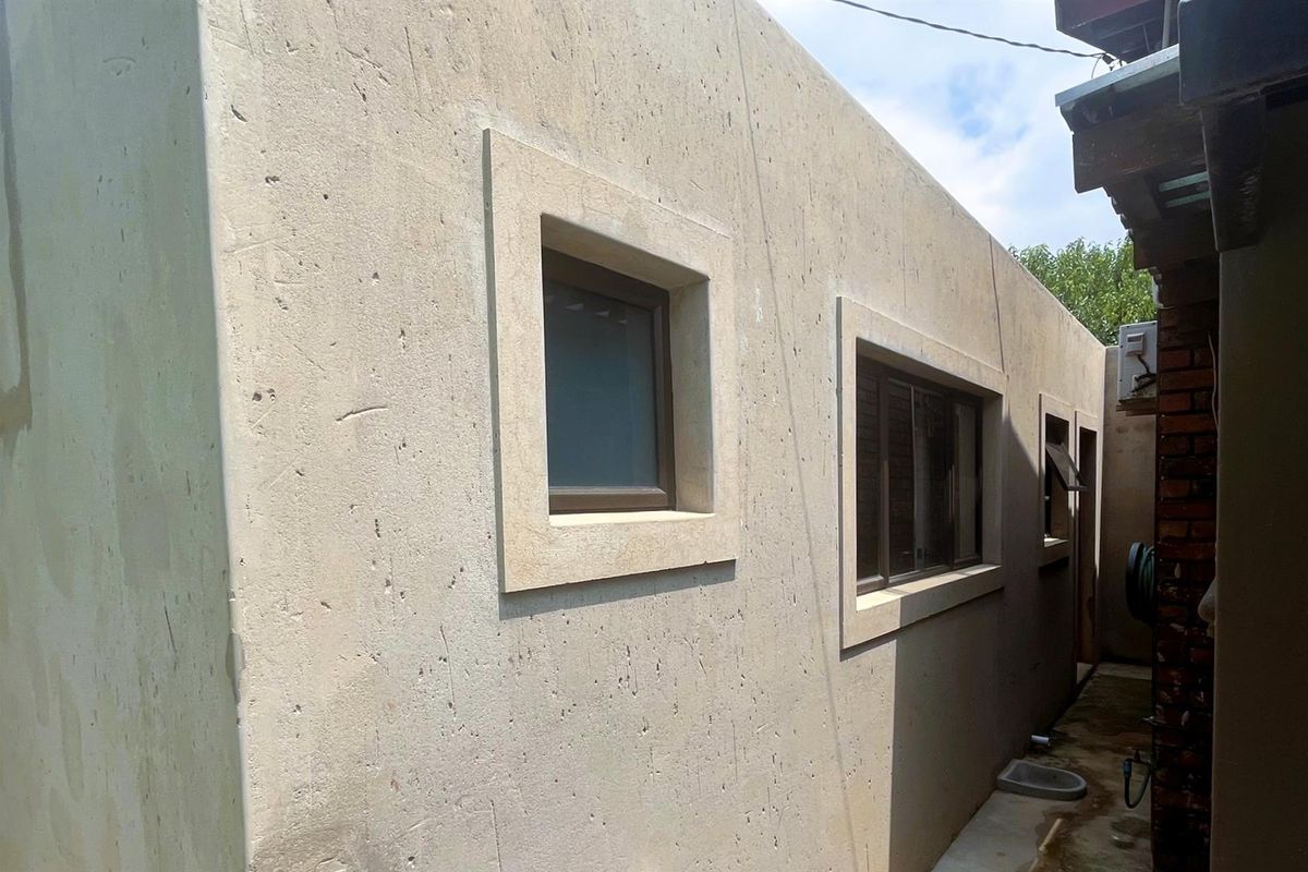 Side exterior view of the property featuring a smooth concrete facade with framed window openings and a narrow paved walkway.