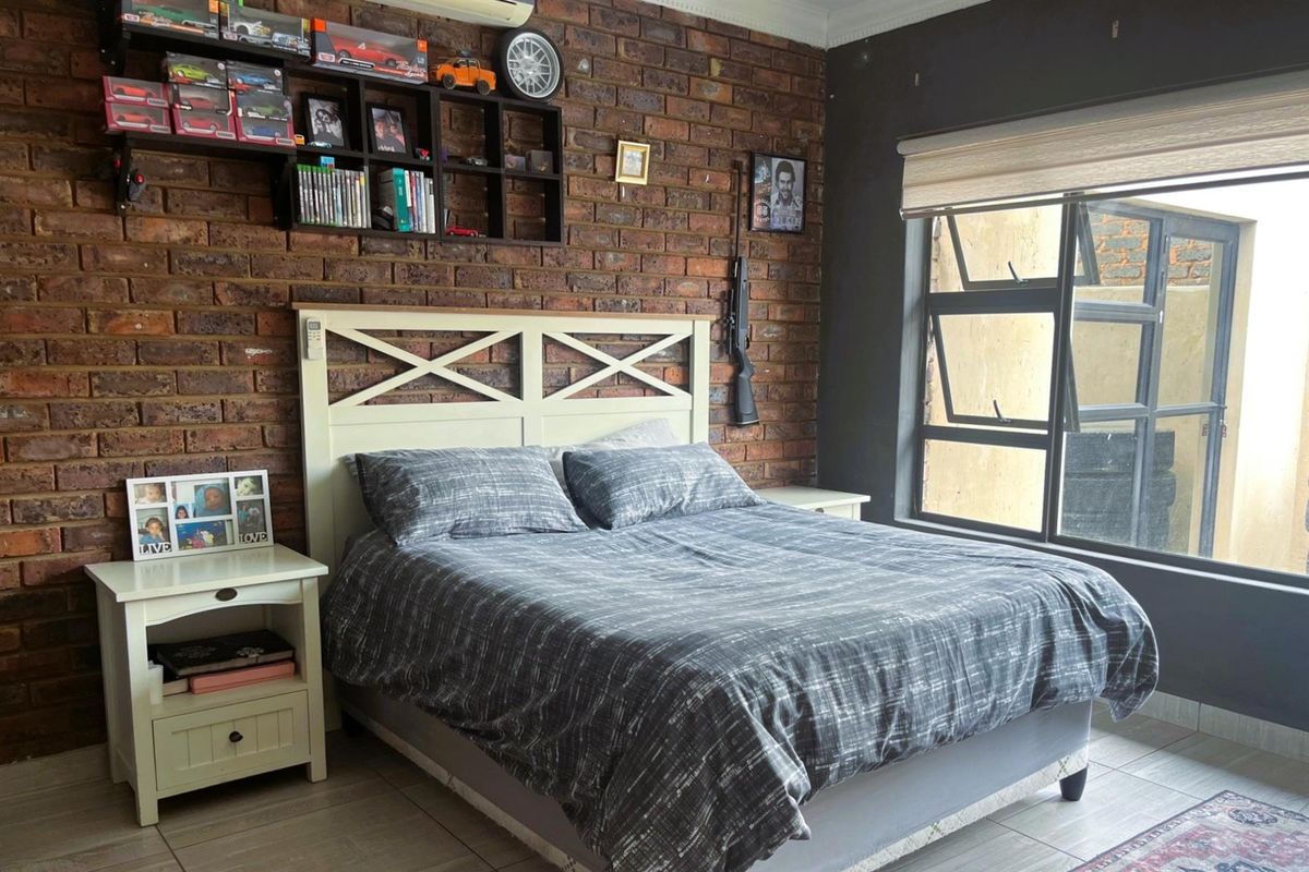 A bedroom featuring an exposed brick feature wall, tiled flooring, and a large window with a roller blind.