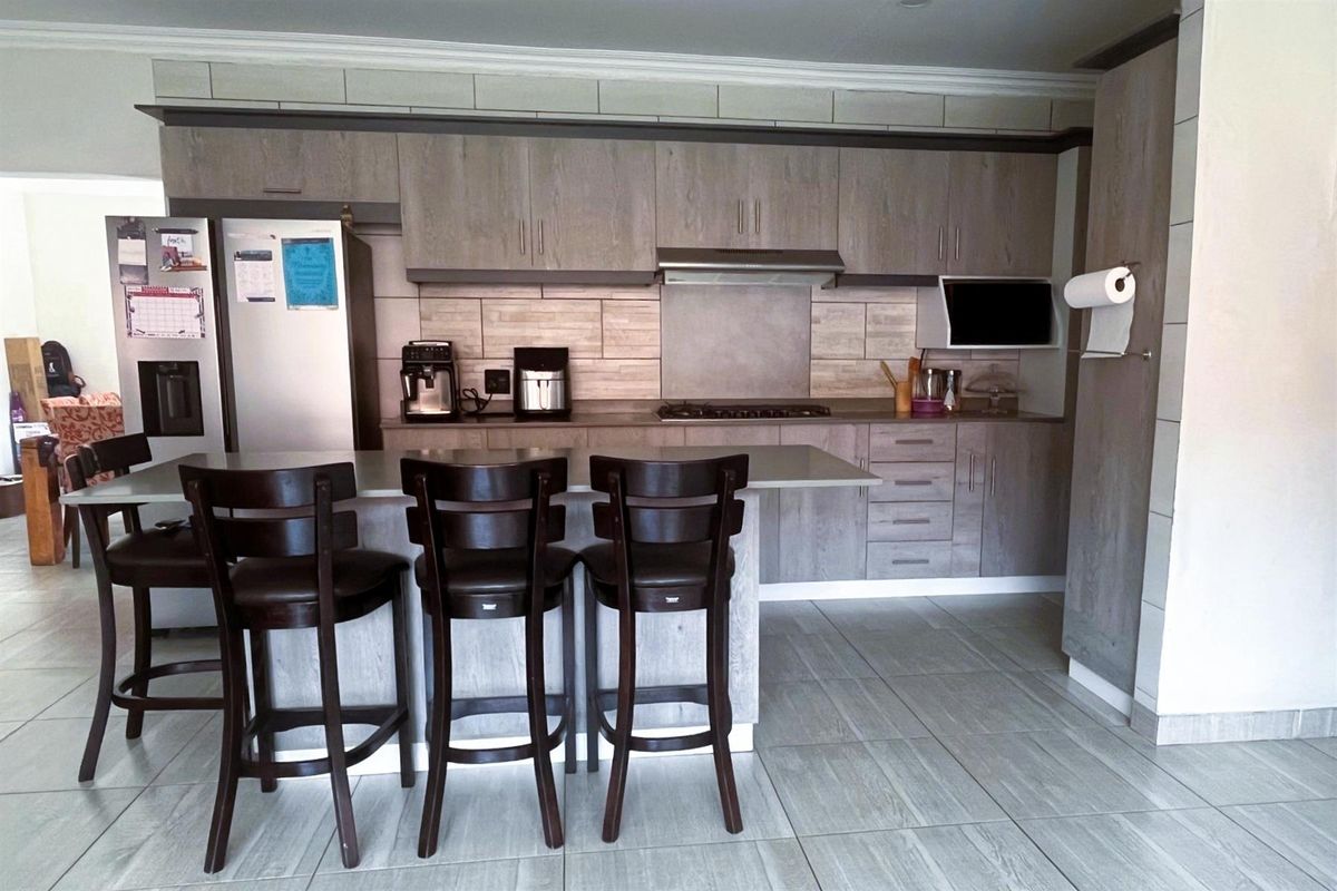 Modern kitchen featuring wood-grain cabinetry, a built-in gas hob with extractor fan, tiled backsplash, and a central breakfast island with stone countertop.