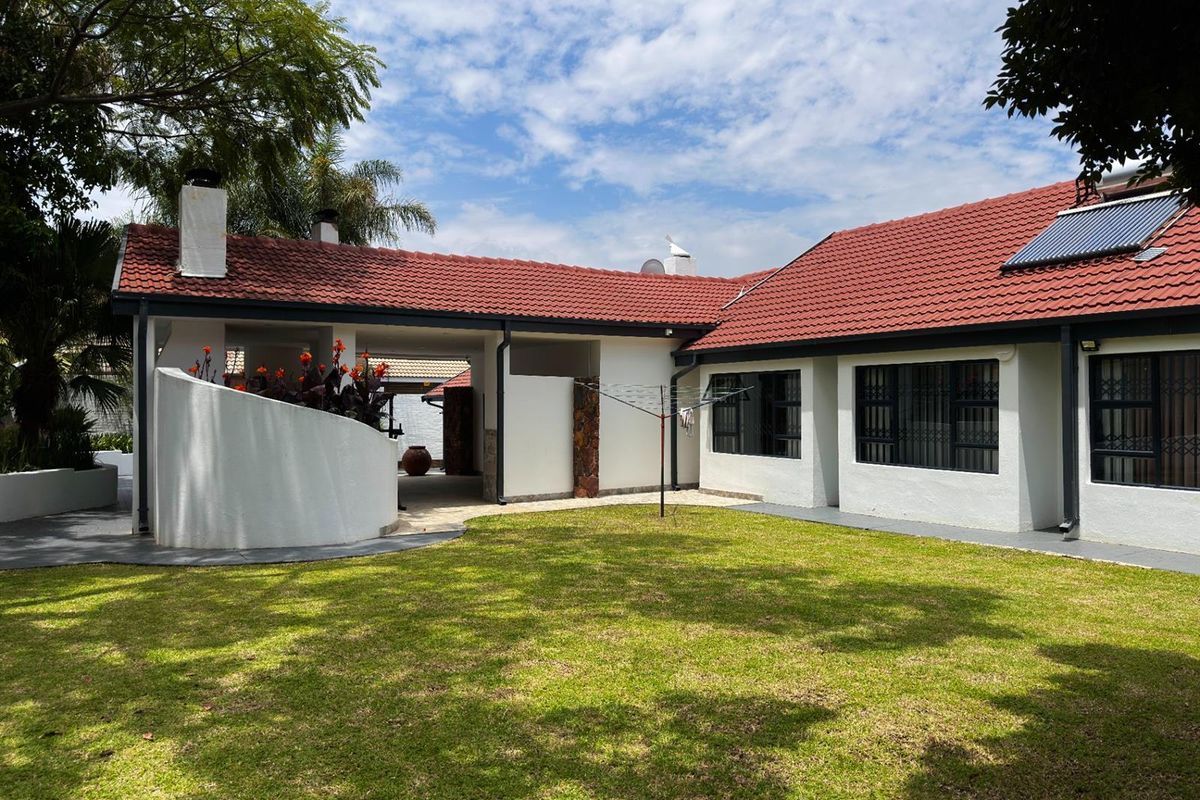 A well-maintained rear exterior view of the house featuring a tiled roof, solar water heating system, and a spacious landscaped garden.