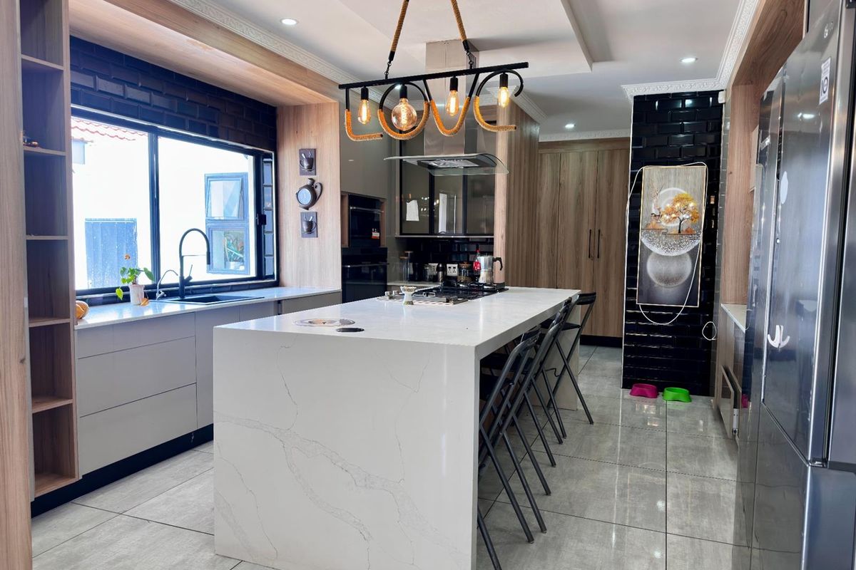 Modern kitchen featuring a large central island with stone countertop, integrated hob, sleek cabinetry, and contemporary pendant lighting.