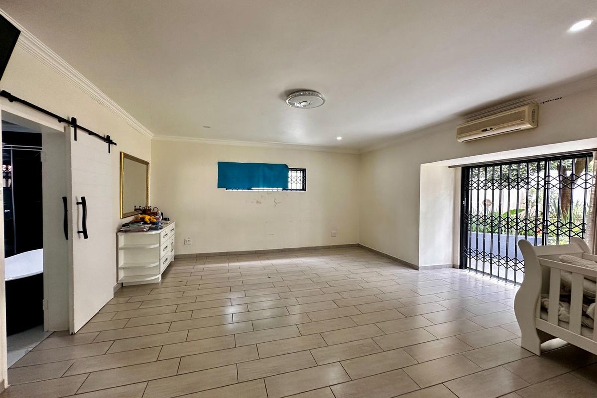 Spacious bedroom featuring tiled flooring, a sliding barn door, wall-mounted air conditioning unit, and security gate access to the exterior.