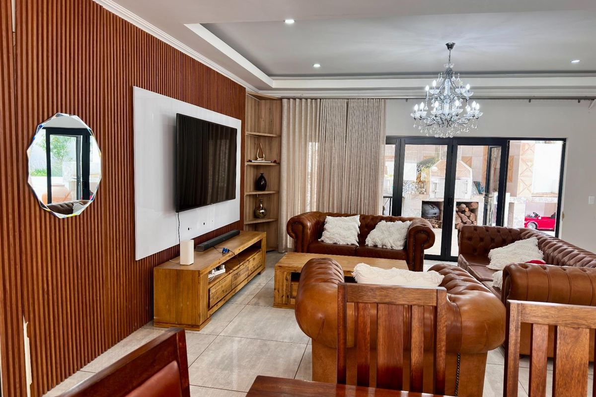 Spacious living area featuring a modern slatted wood feature wall, recessed ceiling lighting, tiled flooring, and large glass sliding doors leading to the patio.