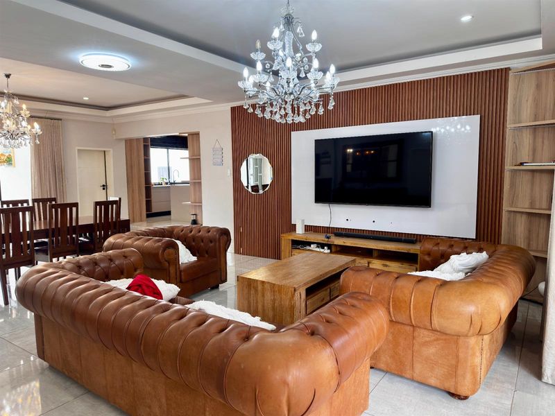 Spacious open-plan living and dining area featuring a modern slatted timber feature wall, built-in media unit, tiled flooring, and elegant crystal chandeliers.