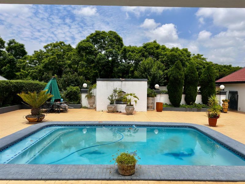 Outdoor pool area featuring a tiled surround, boundary wall, and established garden backdrop, providing a private space for relaxation and entertainment.
