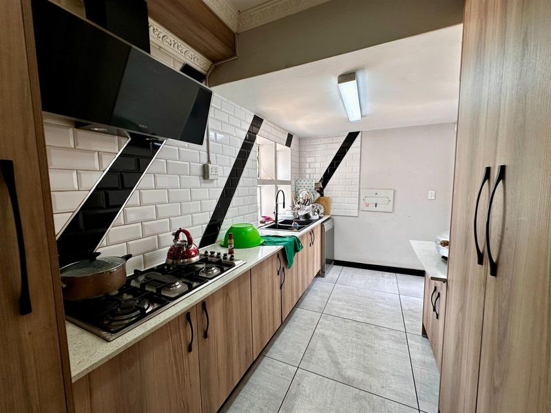 Modern galley-style kitchen featuring wood-finish cabinetry, stone countertops, subway tile backsplash, gas hob, and integrated extractor fan.