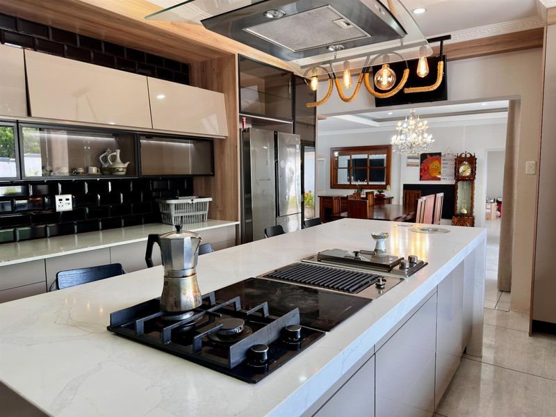Modern open-plan kitchen featuring a large island with integrated gas cooktop and grill, sleek cabinetry, and high-end finishes flowing into the dining area.
