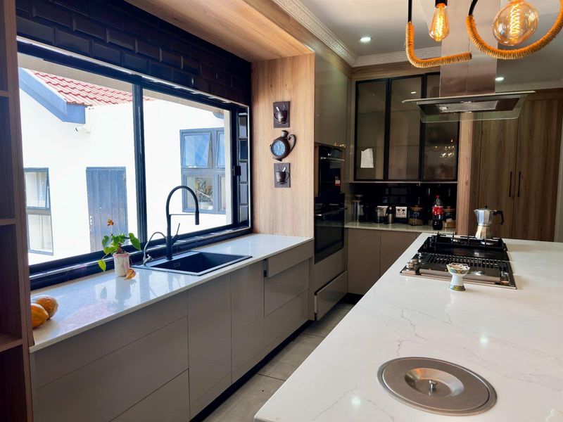 Modern kitchen featuring stone countertops, a central island with a gas hob, built-in oven, and sleek cabinetry with integrated lighting.