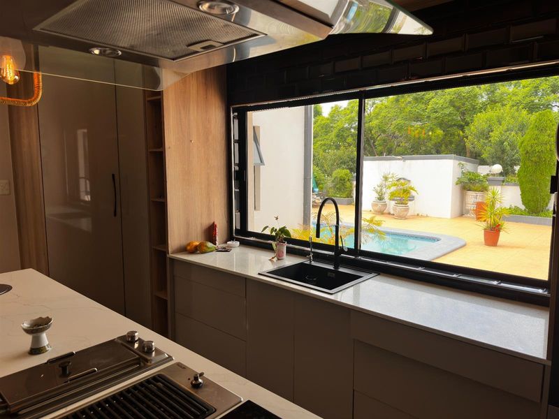 Modern kitchen featuring sleek cabinetry, stone countertops, and a built-in hob, with a large window overlooking the outdoor pool area.