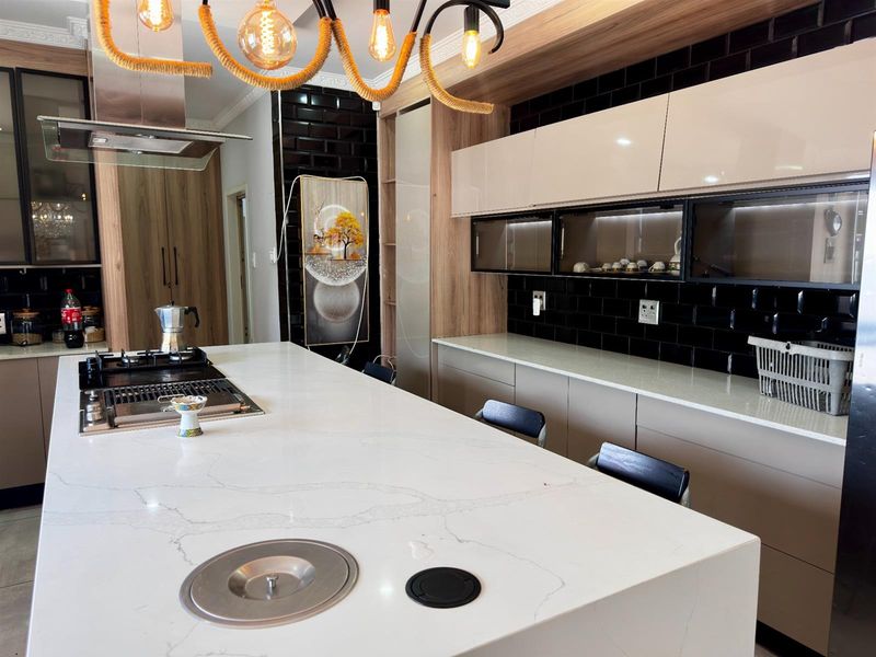 Modern kitchen featuring a large quartz island with integrated hob, sleek gloss cabinetry, and stylish black subway tile backsplash with ambient lighting.
