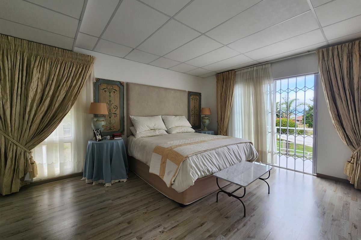 Spacious bedroom featuring wood-look flooring, a suspended ceiling, and large sliding glass doors with security gates leading to an outdoor area.
