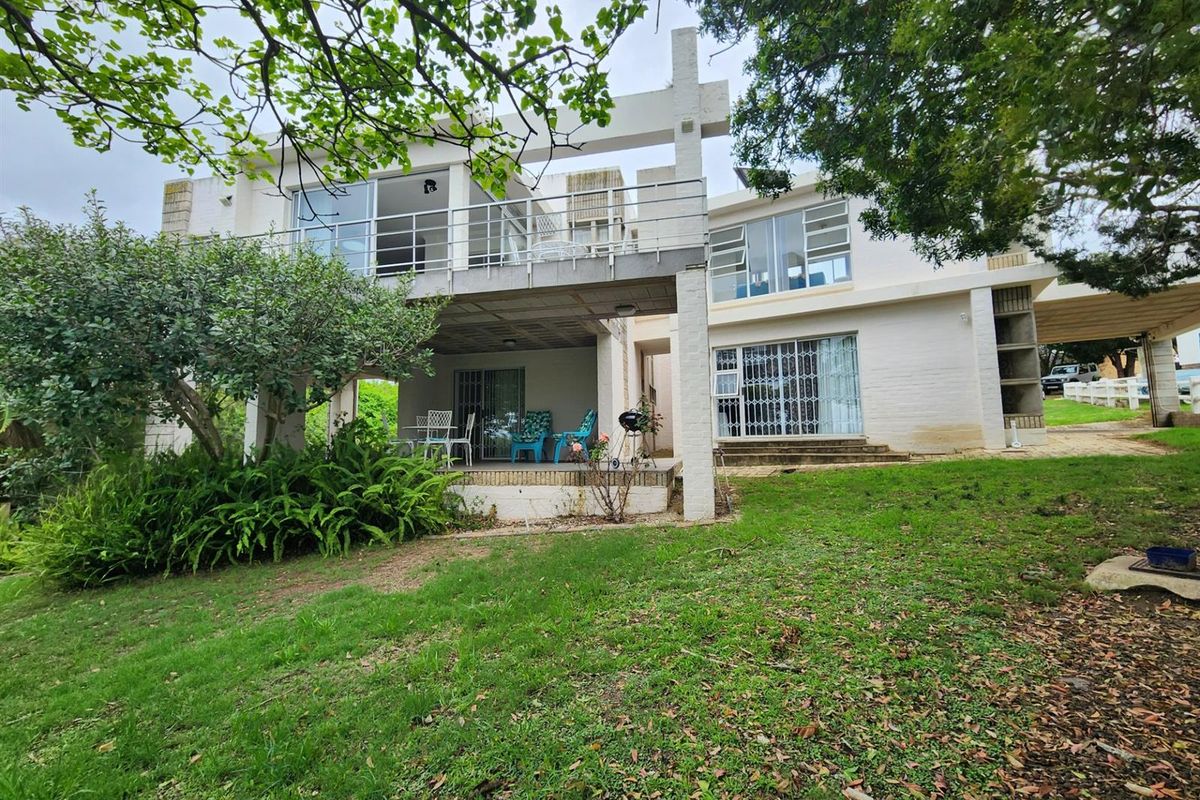 Rear view of a multi-level residential property featuring a covered patio, upper-level balcony with metal railings, and a spacious garden area.