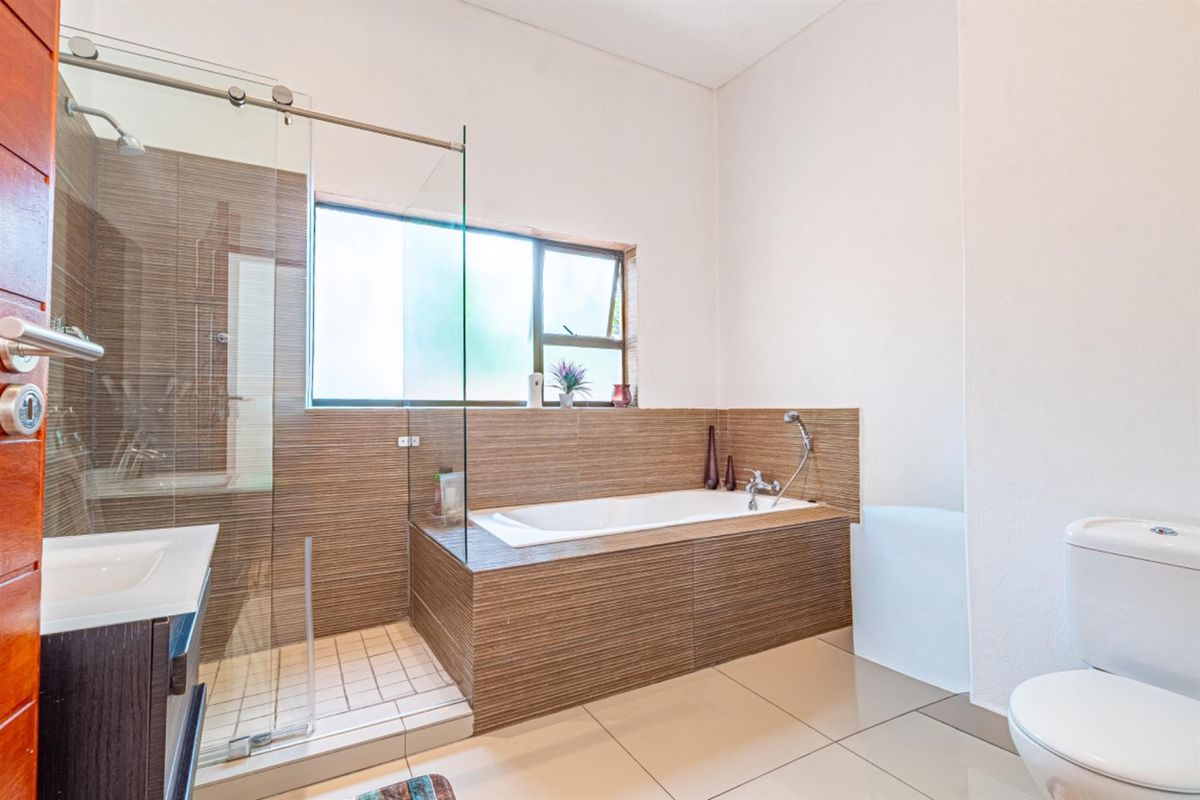 Modern bathroom featuring a glass-enclosed shower, a built-in bathtub with tiled surround, a vanity, and a toilet.