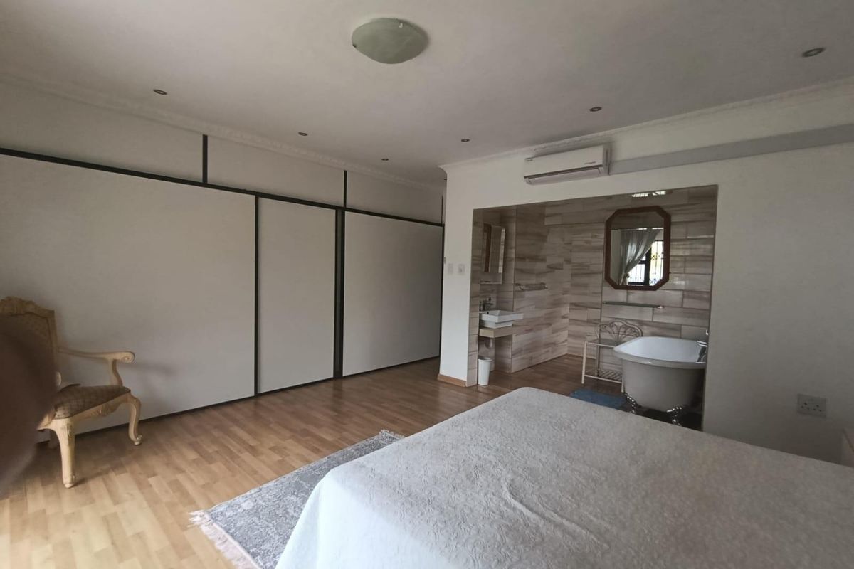 Spacious bedroom featuring laminate flooring, extensive built-in cupboards, and an open-plan en-suite bathroom area with a freestanding bathtub and wall-mounted basin.
