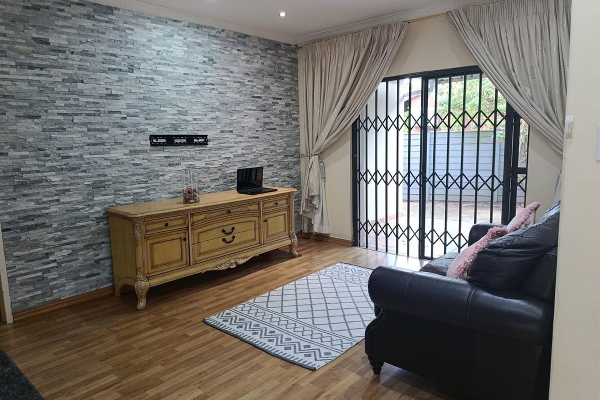 A well-maintained living room featuring a textured stone cladding feature wall, laminate flooring, and direct access to the exterior through a sliding glass door.