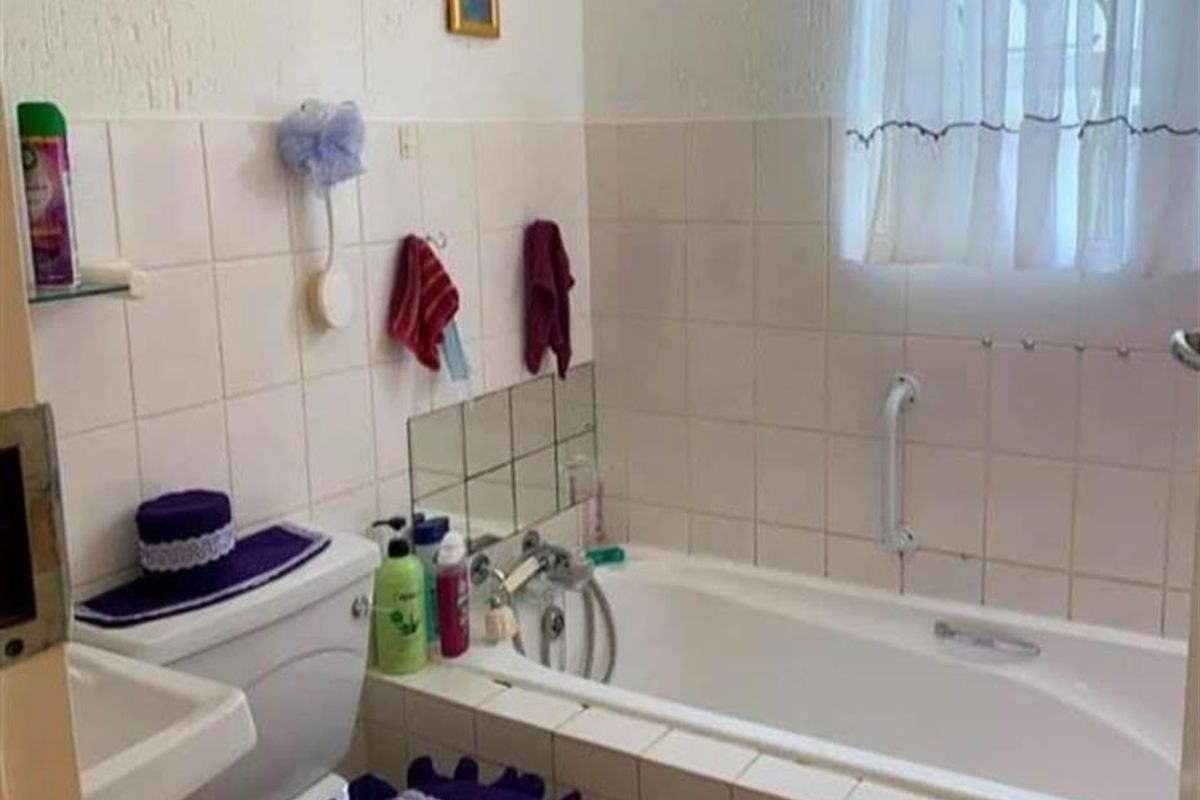 A functional bathroom featuring a built-in bathtub with shower mixer, wall-mounted basin, and toilet, finished with classic white wall tiling.