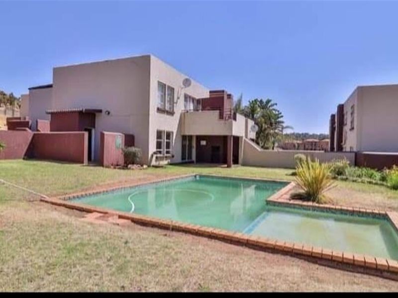 Exterior view of the apartment complex featuring a private swimming pool, paved patio area, and surrounding garden space.
