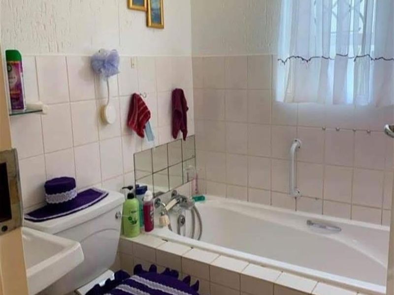 A functional bathroom featuring a built-in bathtub with shower mixer, wall-mounted basin, and toilet, finished with classic white wall tiling.