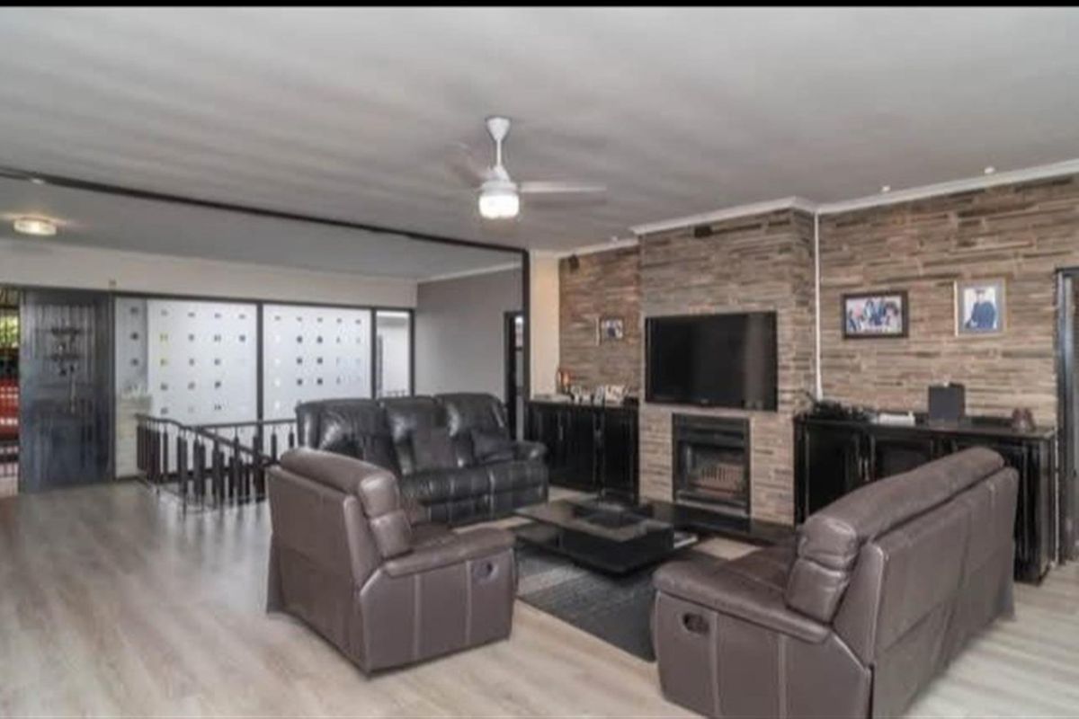 Spacious living room featuring a prominent stone-clad fireplace, laminate flooring, and a ceiling fan, creating a warm and inviting atmosphere.