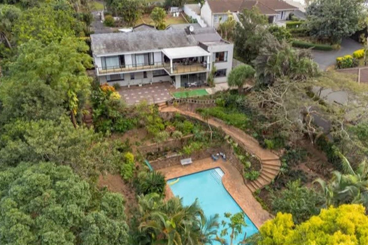 Aerial view of a multi-level residential property featuring a swimming pool, terraced garden, paved patio area, and a spacious upper-level balcony.