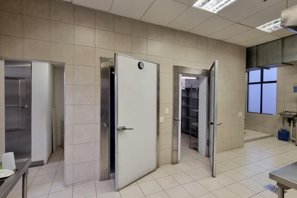 Commercial kitchen area featuring tiled surfaces, integrated walk-in cold storage units, stainless steel sink, and industrial extractor hood.