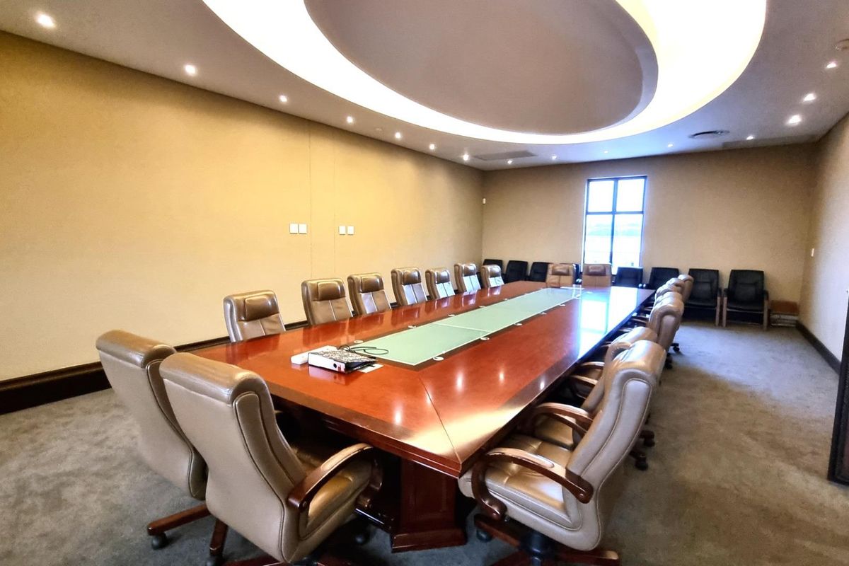 A spacious commercial boardroom featuring a large conference table, recessed ceiling lighting with cove accents, and carpeted flooring.