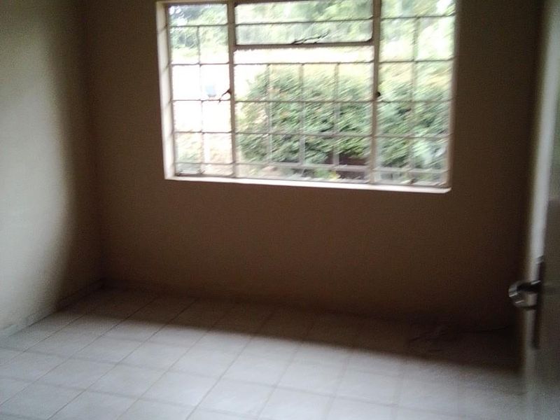An empty bedroom featuring tiled flooring, a window with security bars, and simple cove cornicing.