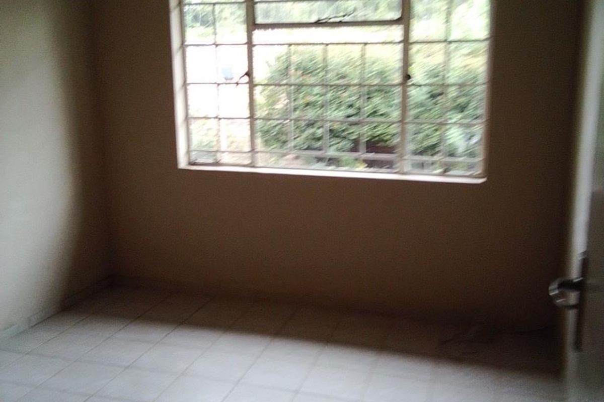 An empty bedroom featuring tiled flooring, a window with security bars, and simple cove cornicing.