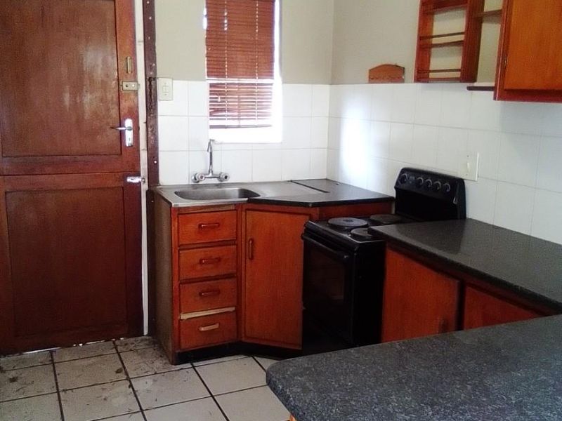 A compact kitchen featuring wooden cabinetry, laminate countertops, a freestanding stove, and tiled flooring, offering a functional layout ready for modernization.