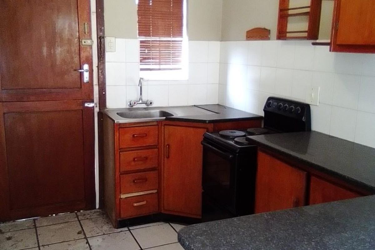 A compact kitchen featuring wooden cabinetry, laminate countertops, a freestanding stove, and tiled flooring, offering a functional layout ready for modernization.